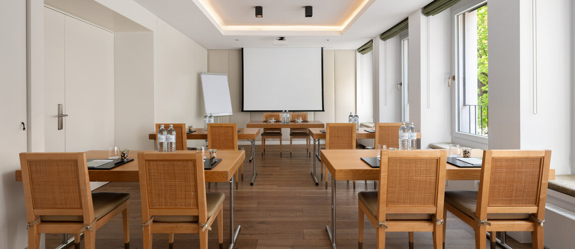 Heller Tagungsraum mit Leinwand und Holzmöbeln.