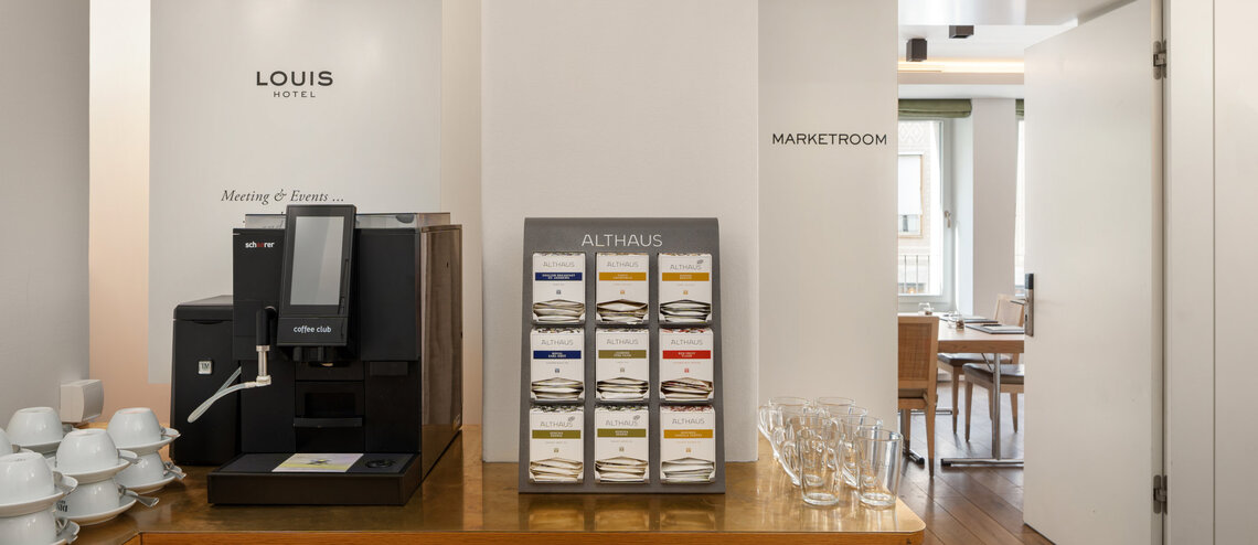 Ein Kaffeeautomat und eine Auswahl an Tee steht vor einem Tagungsraum bereit.