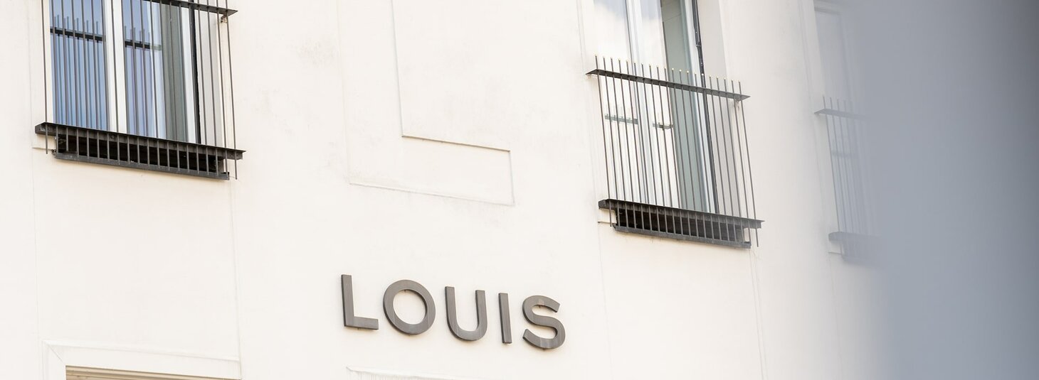 Façade of the LOUIS Hotel in Munich with large windows and balcony grilles.
