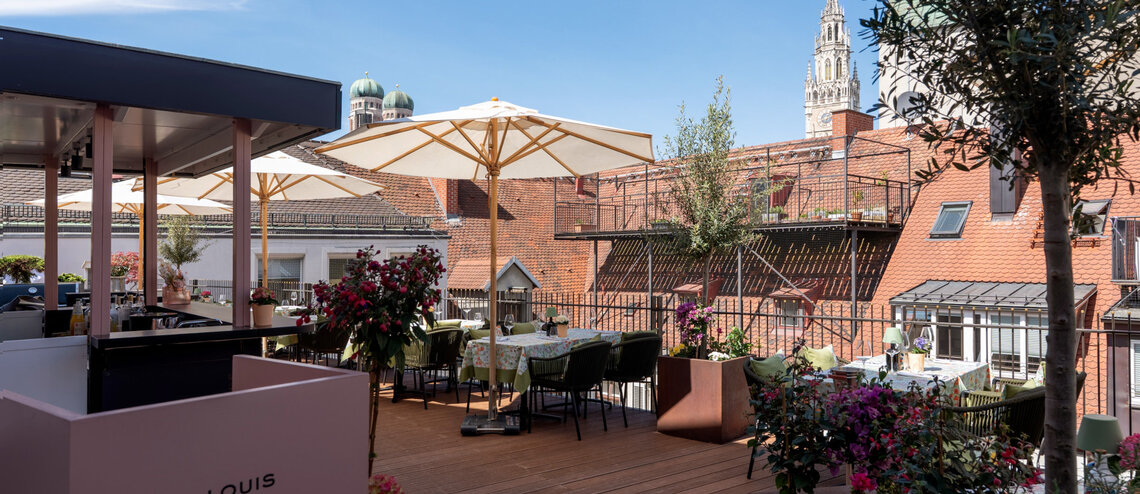 : © Tony Gigov The roof walkway, lined with flowers and offering a view of the surrounding rooftops against a blue sky.
