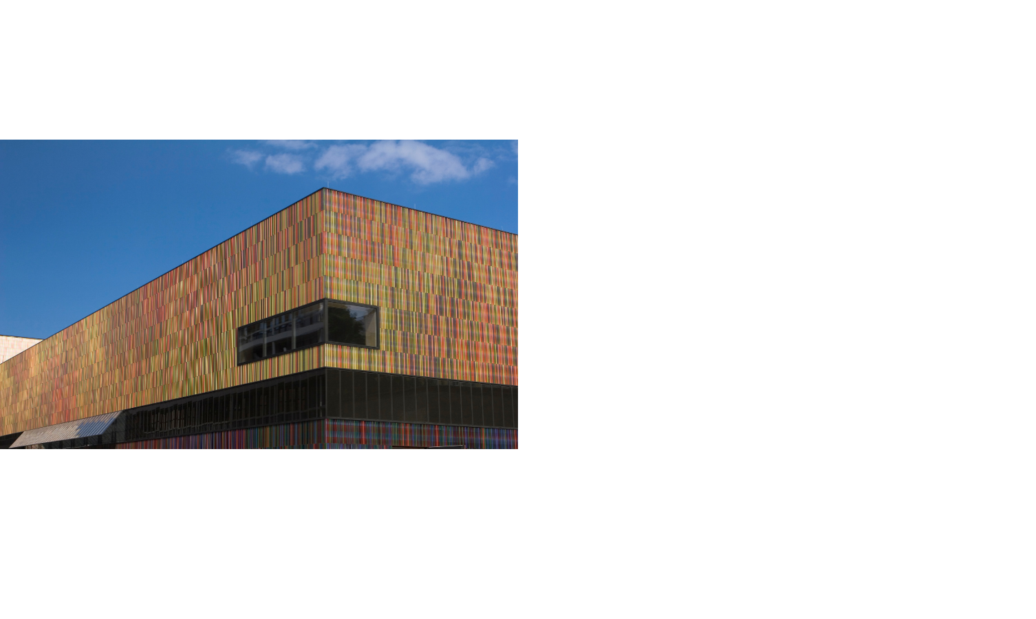 Buntes, modernes Gebäude mit Streifenfassade und blauem Himmel im Hintergrund.