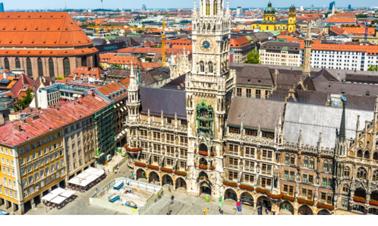Luftaufnahme des Münchner Rathauses mit roten Dächern und umliegenden historischen Gebäuden bei klarem Himmel.