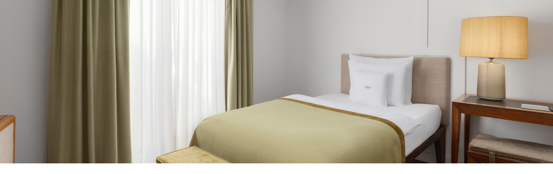 Gemütliches Hotelzimmer mit Einzelbett, grüner Tagesdecke und warmem Licht.