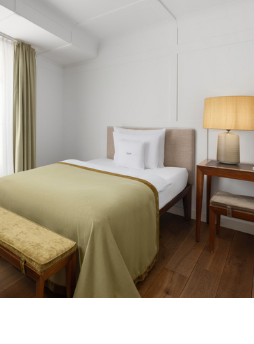 A cosy hotel room with a single bed, a green bedspread and warm lighting.