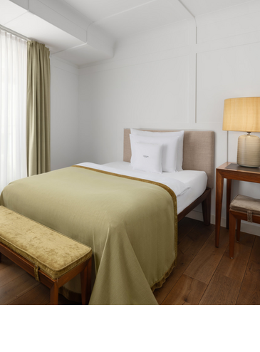 Gemütliches Hotelzimmer mit Einzelbett, grüner Tagesdecke und warmem Licht.