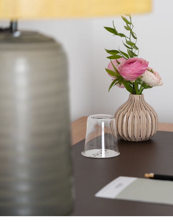 Nachttisch mit Blumenvase, Wasserglas und Notizblock.