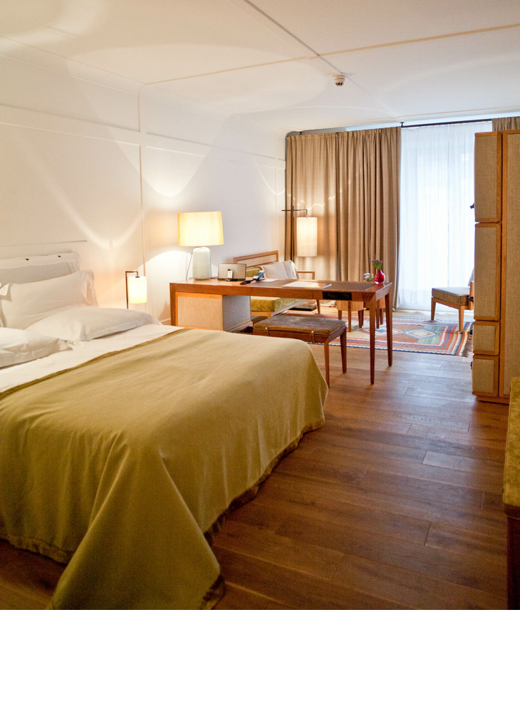 Comfortable hotel room with double bed, desk, armchairs and large windows with curtains at the LOUIS Hotel Munich.