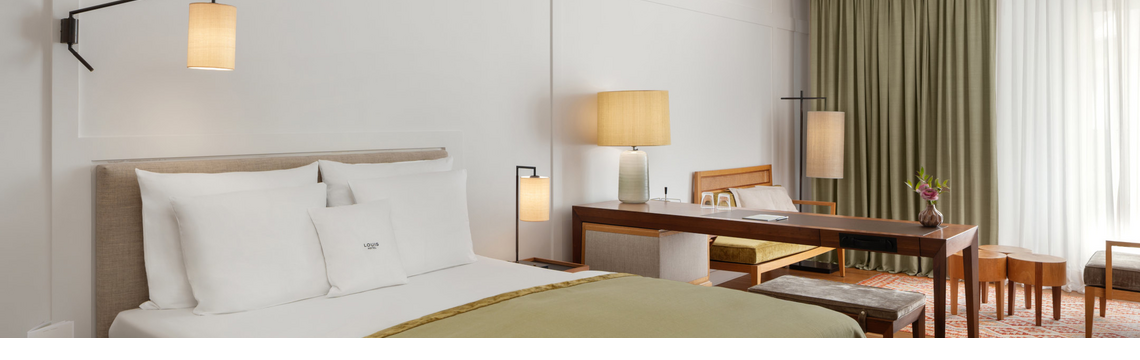 Gemütliches Hotelzimmer mit Doppelbett, Schreibtisch, Sesseln und großen Fenstern mit Vorhängen im LOUIS Hotel München.
