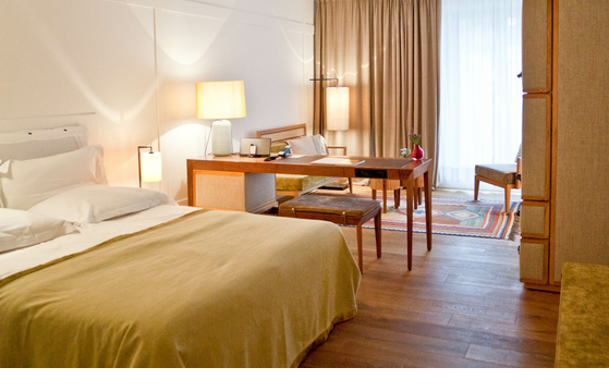 Comfortable hotel room with double bed, desk, armchairs and large windows with curtains at the LOUIS Hotel Munich.