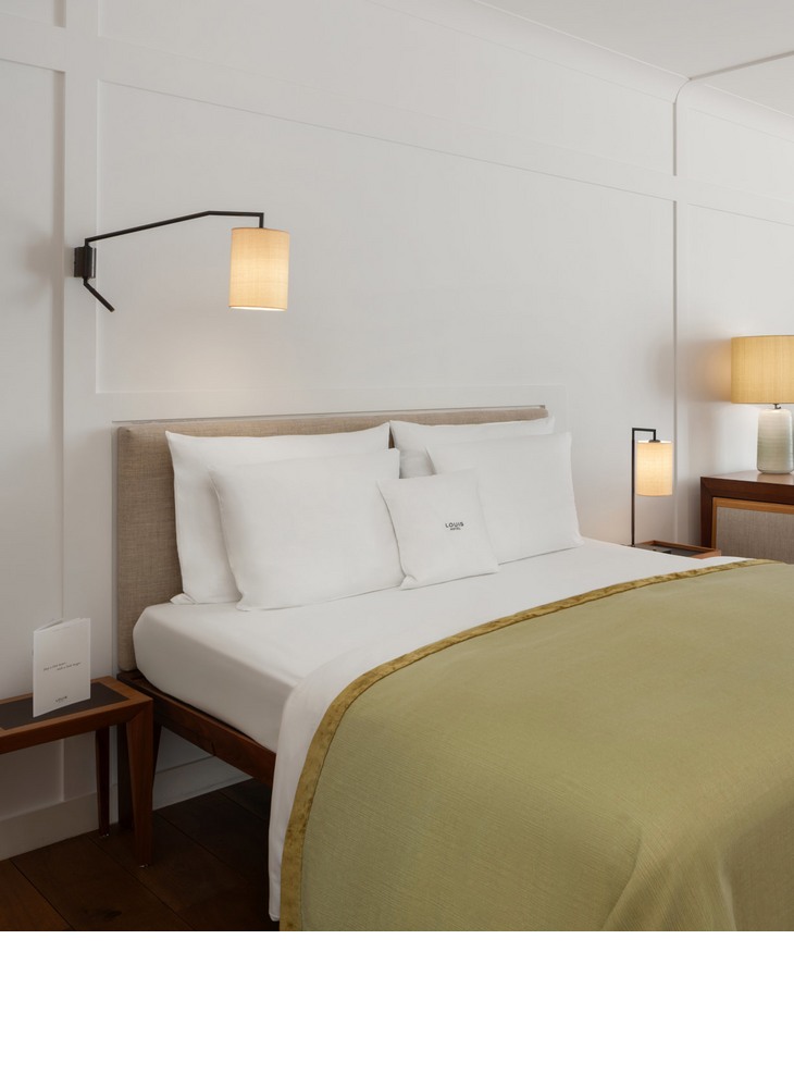 Comfortable hotel room with double bed, desk, armchairs and large windows with curtains at the LOUIS Hotel Munich.