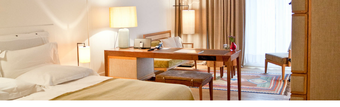 Gemütliches Hotelzimmer mit Doppelbett, Schreibtisch, Sesseln und großen Fenstern mit Vorhängen im LOUIS Hotel München.