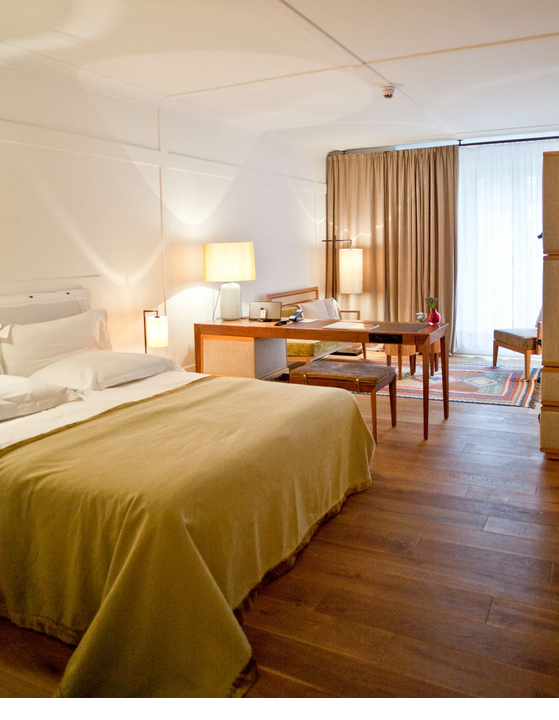 Comfortable hotel room with double bed, desk, armchairs and large windows with curtains at the LOUIS Hotel Munich.