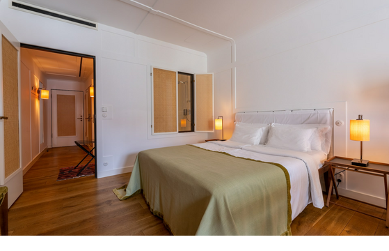 Modern hotel room with double bed, wooden floor, warm light and open bathroom window at the LOUIS Hotel Munich.