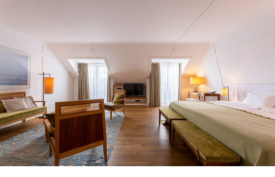Helles Hotelzimmer mit Holzboden, Doppelbett, Sitzbereich, TV und großen Fenstern mit Vorhängen im LOUIS Hotel München.