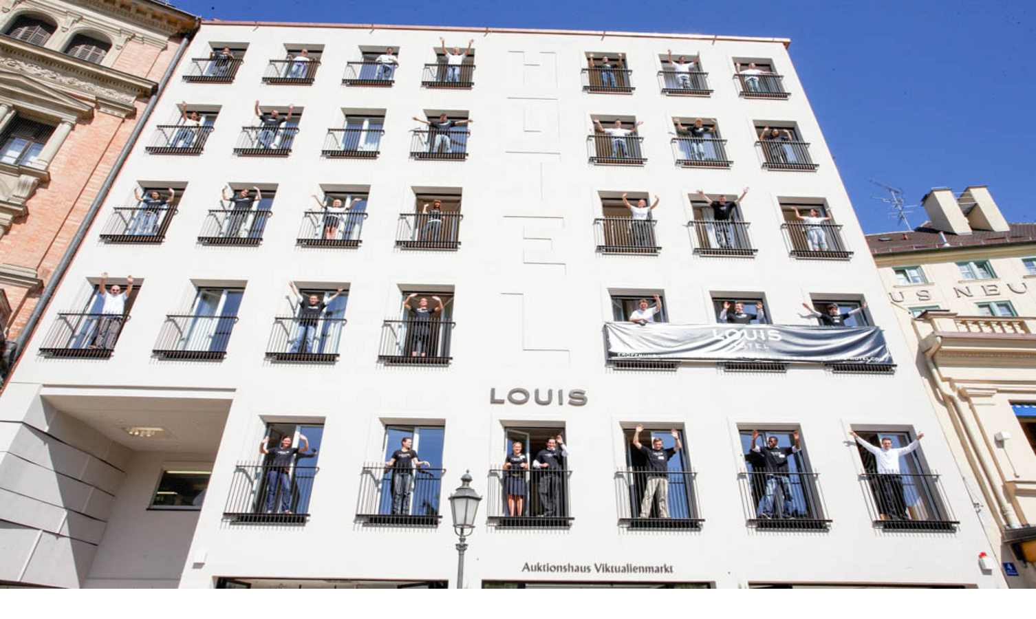 Exterior view LOUIS Hotel Munich Façade of the LOUIS Hotel in Munich with people on balconies waving in a friendly manner.