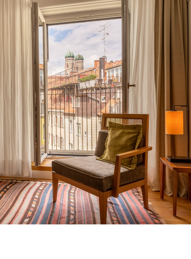 Cozy hotel room with open balcony door and view of the towers of the Frauenkirche in Munich.