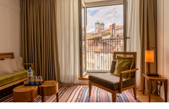 Cozy hotel room with open balcony door and view of the towers of the Frauenkirche in Munich.