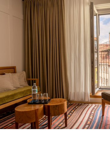 Cozy hotel room with open balcony door and view of the towers of the Frauenkirche in Munich.