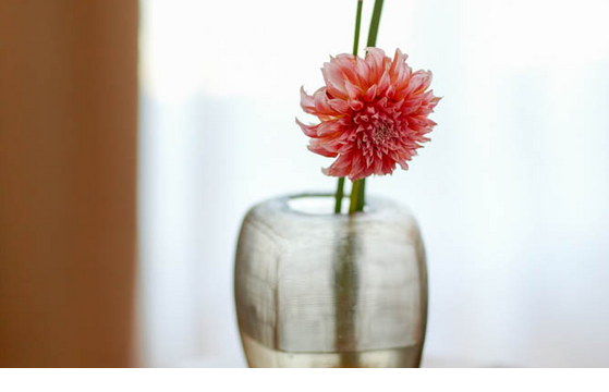 Blumenvase auf dem Zimmer LOUIS Hotel Muenchen Einzelne rosa Blume in einer Glasvase auf einem Holztisch vor einem hellen Hintergrund im LOUIS Hotel München.