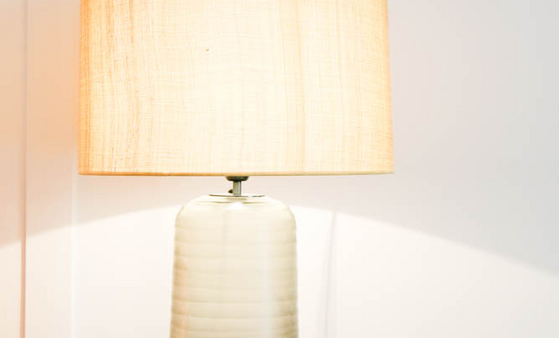 Tischlampe mit hellem Schirm auf Holztisch, daneben ein Telefon und Infokarte im LOUIS Hotel München.