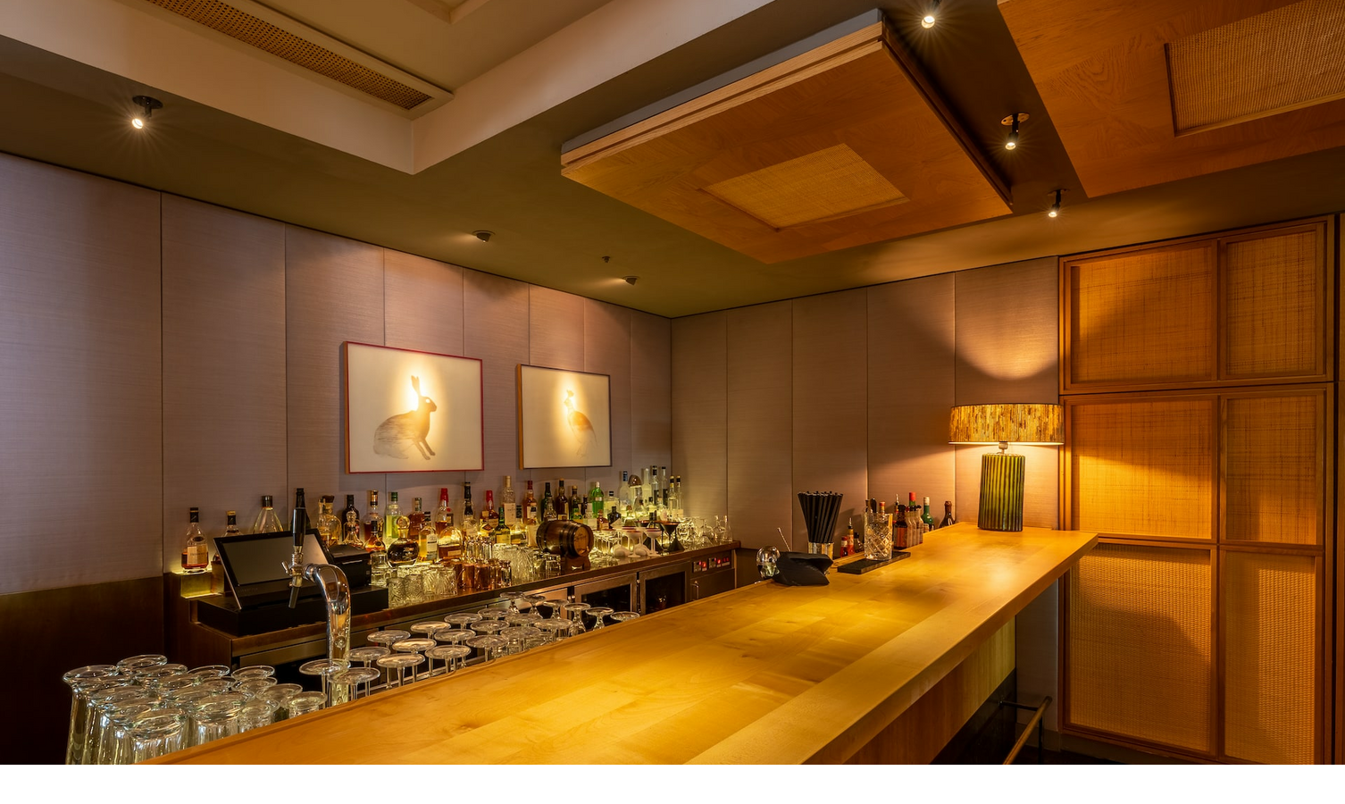Elegant hotel bar in the LOUIS Hotel Munich with wooden counter, glasses and atmospheric lighting.