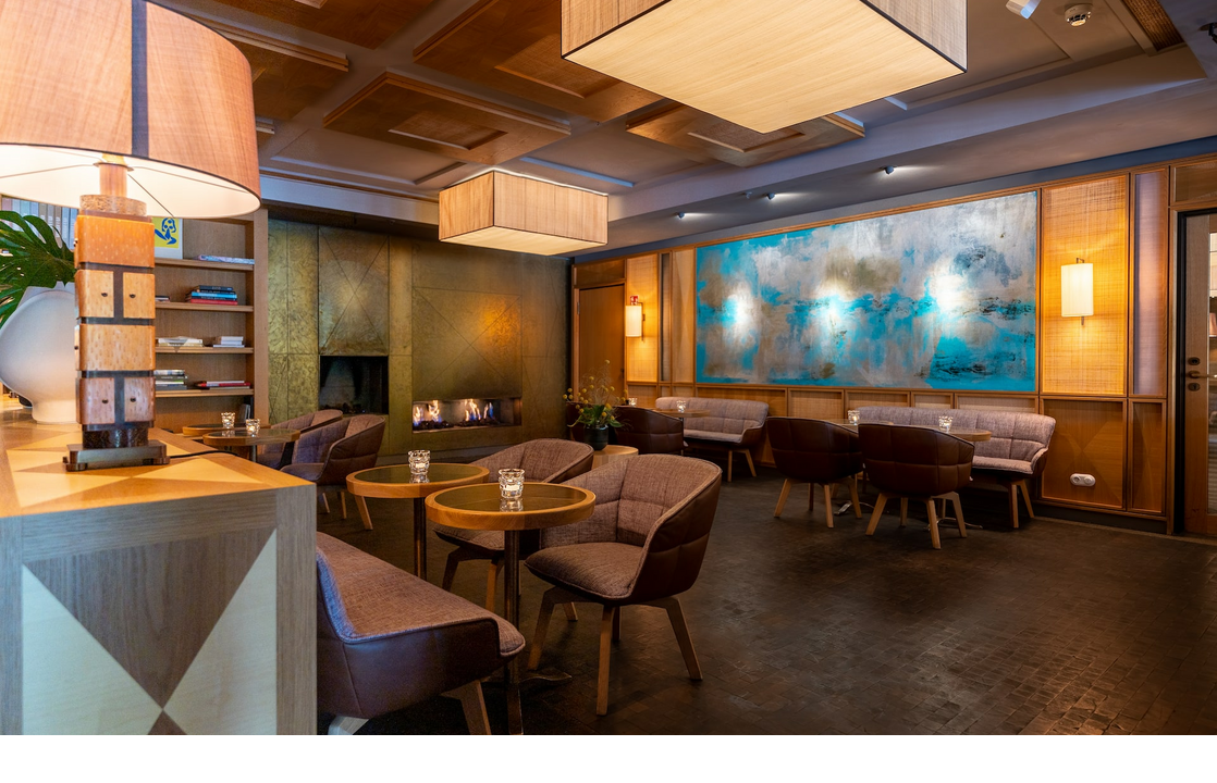 Elegante Hotel-Lounge mit modernen Sesseln, Holztischen, Kamin und großem, abstrakten Wandgemälde in Blau- und Brauntönen.