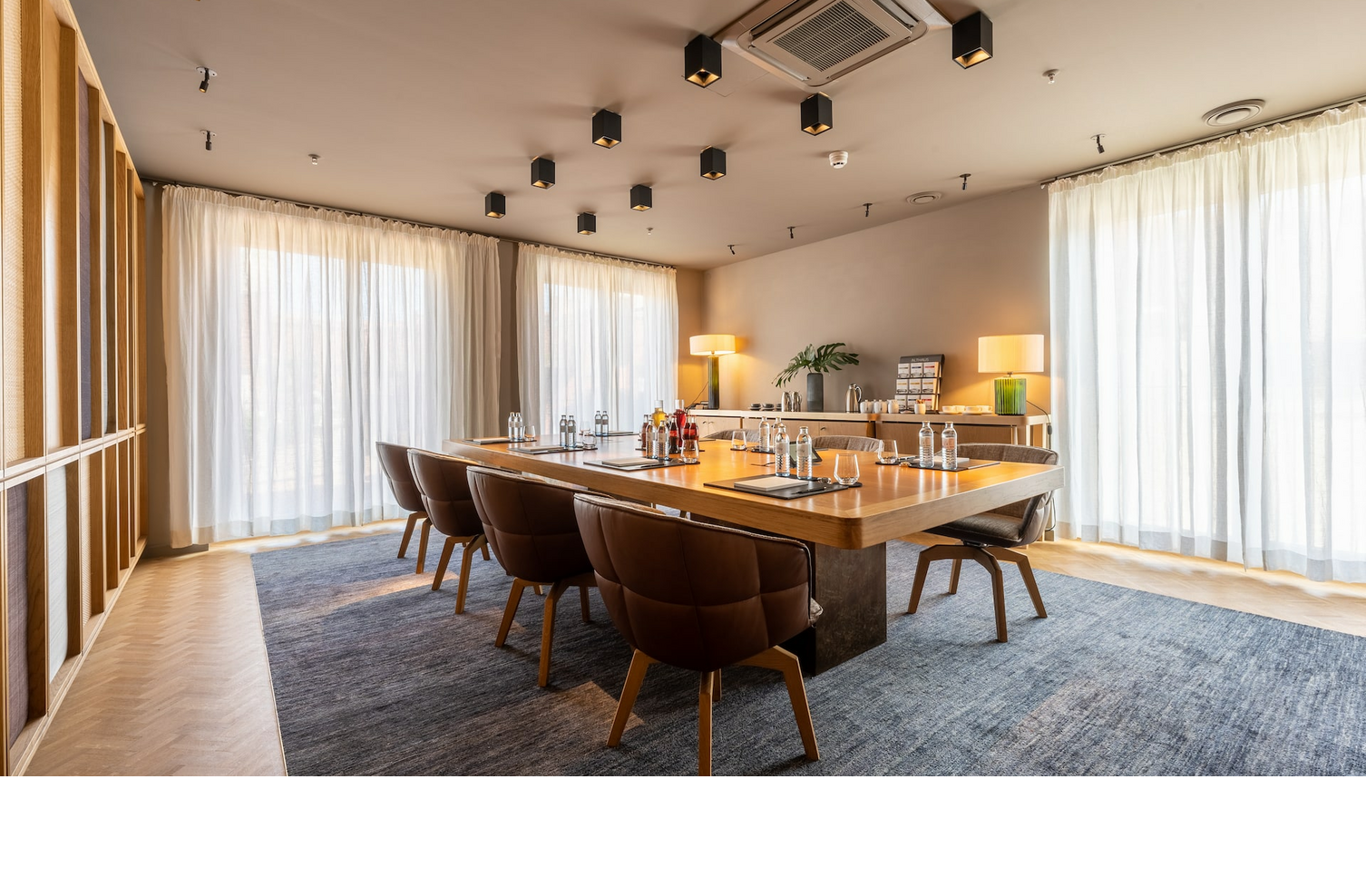 Moderner Konferenzraum im LOUIS Hotel München mit großem Tisch, eleganten Stühlen und Tageslicht durch bodenlange Fenster.