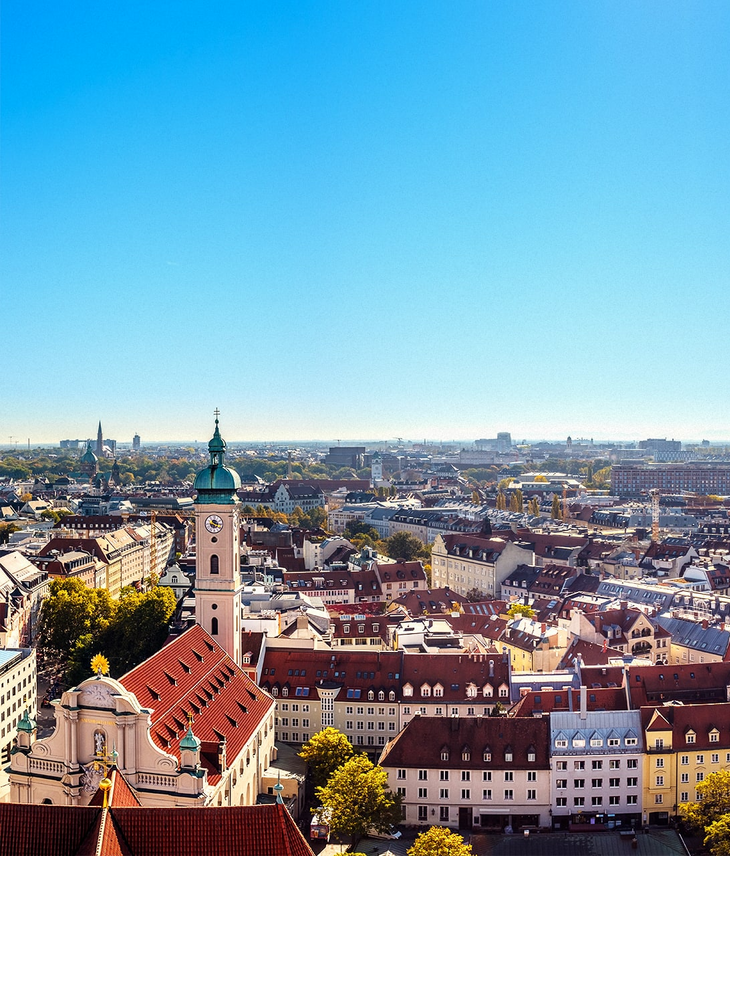 City view of Munich under a clear sky, with church tower and colorful buildings in the foreground.