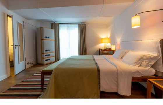 Modern hotel room with large bed, wooden floor, stylish lighting, closet and desk by the window.