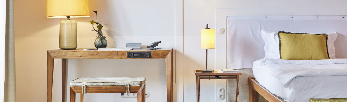 Bright hotel room with wooden furniture, bed, desk, lamps and decoration in the LOUIS Hotel Munich.