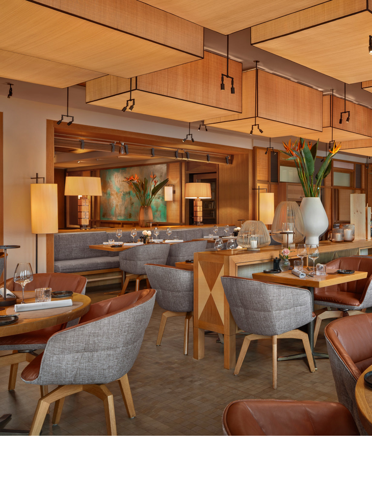 Elegantes Restaurant im LOUIS Hotel München mit stilvollen Holztischen, gemütlichen Sesseln und warmem Lichtambiente.