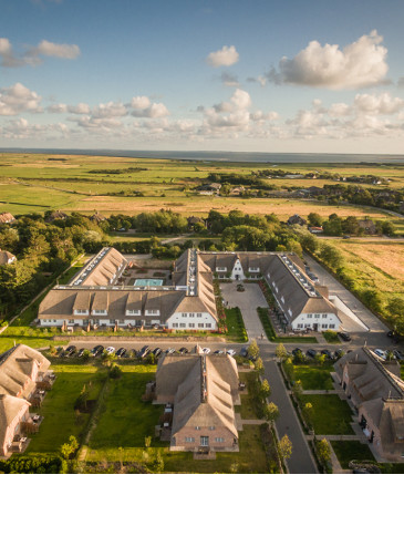 Luftaufnahme des Severin*s Resort & Spa auf Sylt, umgeben von grüner Landschaft und malerischem Himmel.