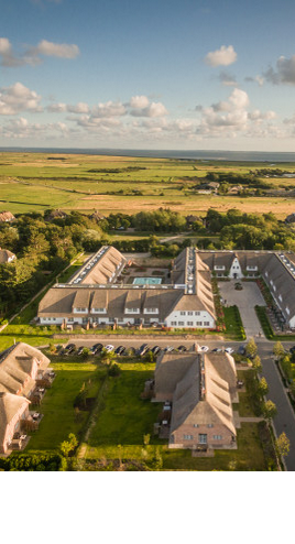 Luftaufnahme des Severin*s Resort & Spa auf Sylt, umgeben von grüner Landschaft und malerischem Himmel.