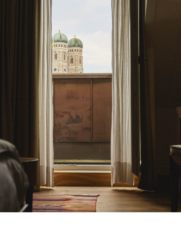 Blick aus einem Hotelzimmer auf die Türme der Frauenkirche durch ein Fenster mit halb geöffneten Vorhängen.
