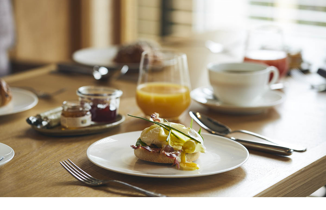 Breakfast table with Eggs Benedict, orange juice, coffee and jam at the LOUIS Hotel Munich.