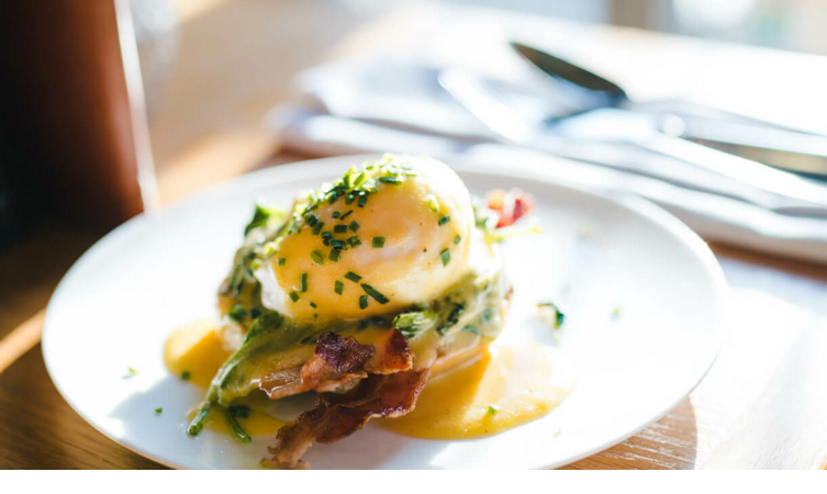Ein elegantes Frühstücksgericht mit pochiertem Ei, Sauce und Schnittlauch auf einem weißen Teller im LOUIS Hotel München.
