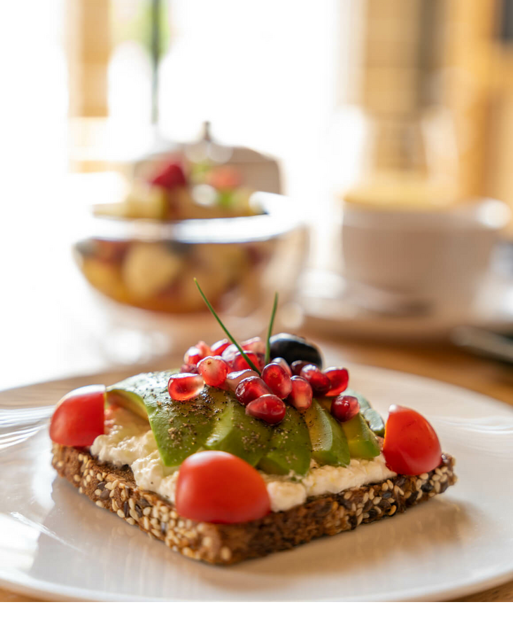 Wholemeal bread with avocado, cream cheese, pomegranate seeds and tomatoes on a white plate at the LOUIS Hotel Munich.