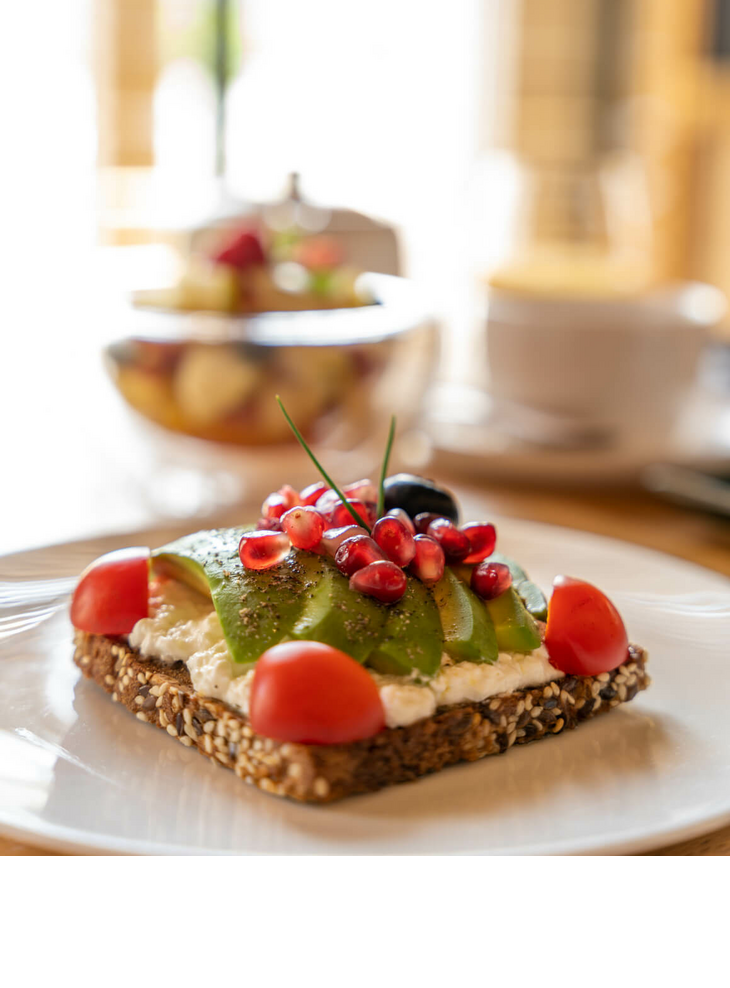 Wholemeal bread with avocado, cream cheese, pomegranate seeds and tomatoes on a white plate at the LOUIS Hotel Munich.