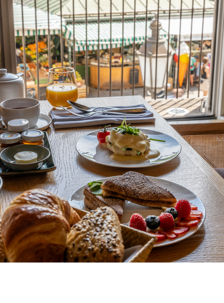 Frühstückstisch im LOUIS Hotel mit Croissants, Obst, Saft und Blick auf den Viktualienmarkt in München.