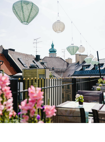 View from the hotel terrace with flowers, hanging lamps and church tower in the background.