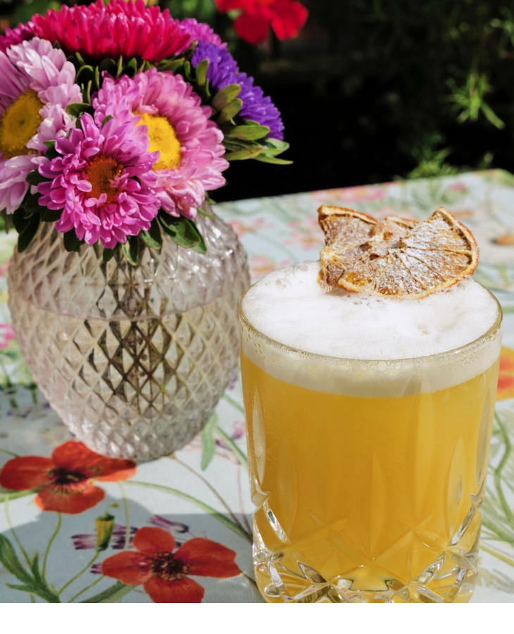 Bouquet of flowers in vase and cocktail with dried lemon on floral table.
