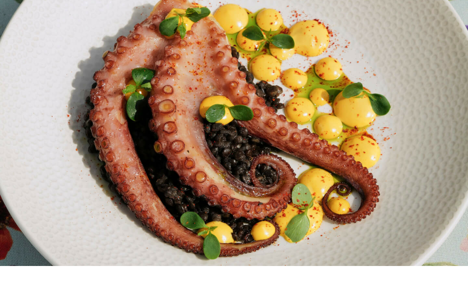 Gegrillter Oktopus auf schwarzem Reis mit gelber Sauce, serviert auf einem blumigen Tisch.
