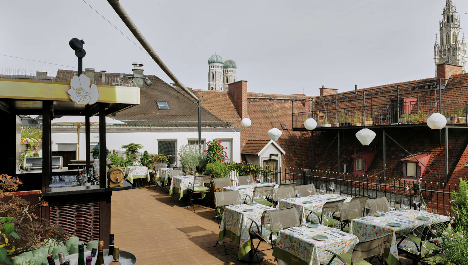 Dachterrasse des LOUIS Hotels München mit gedeckten Tischen, Pflanzen und Blick auf die Türme der Frauenkirche.