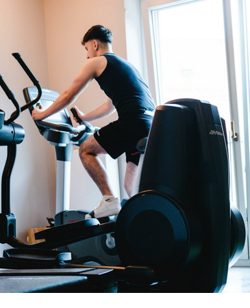 LOUIS Fitness im 6. Stock des LOUIS Hotels München Ein Mann trainiert auf einem Heimtrainer im Fitnessraum des LOUIS Hotel München.