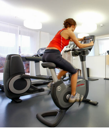 Frau trainiert auf Fahrrad im Fitnessraum des LOUIS Hotels München