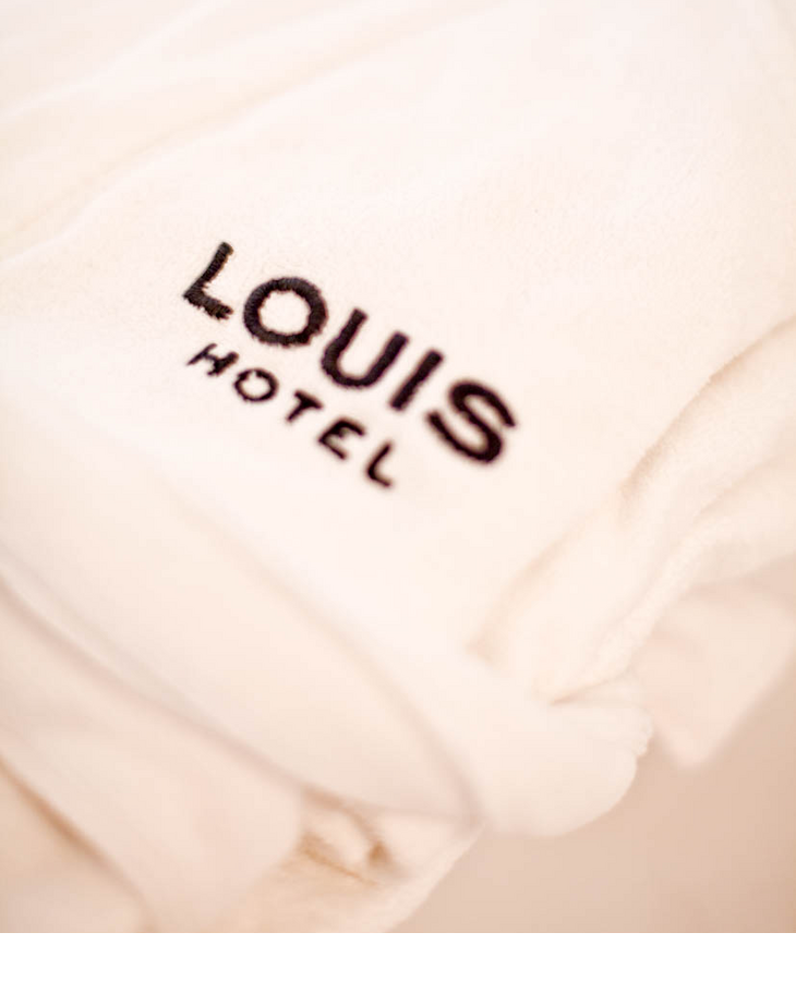 Bademantel und Handtücher l LOUIS Hotel in München Weißer Hotelbademantel mit schwarzem LOUIS Hotel-Logo, weich und luxuriös.