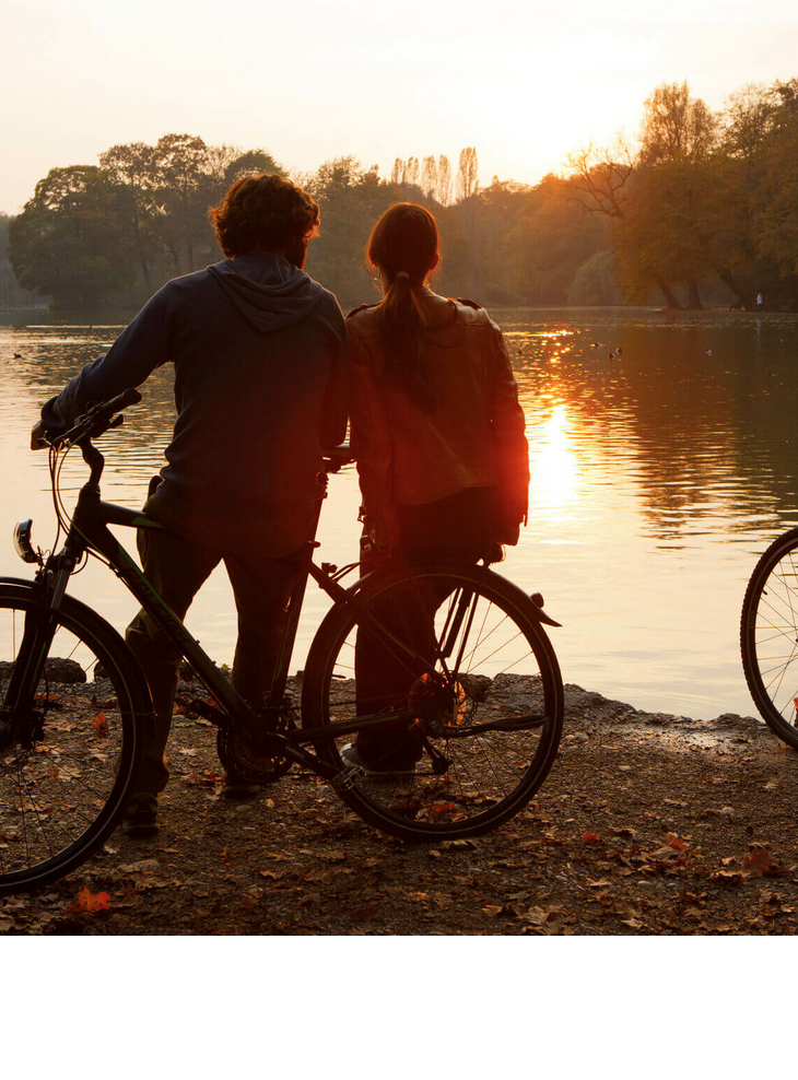 Bike tour in autumn Two people with bicycles stand on the lakeshore and enjoy the sunset.