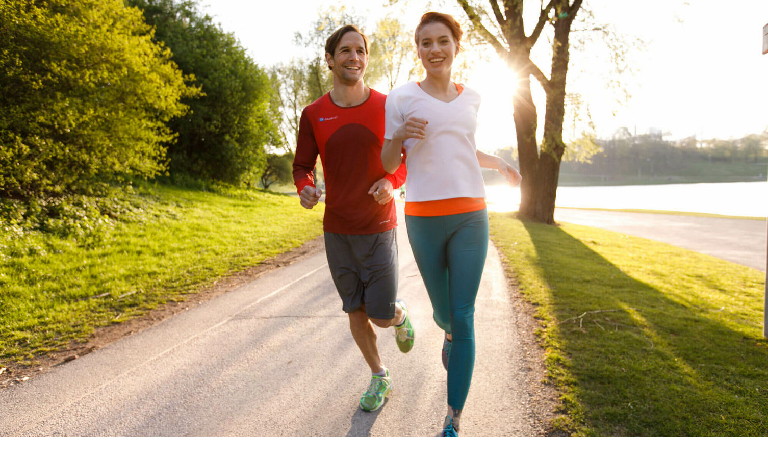 Two people are jogging along a sunny park path, surrounded by trees and green spaces.