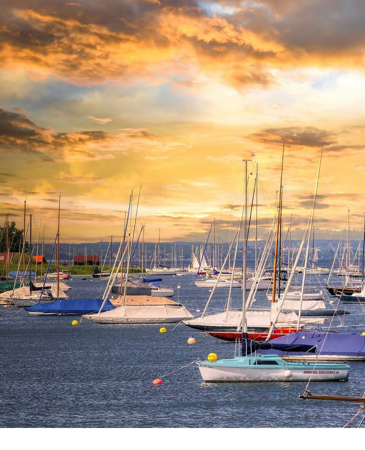 Ammersee in München Segelboote im Hafen bei Sonnenuntergang, umgeben von ruhigem Wasser und einem dramatischen Himmel.