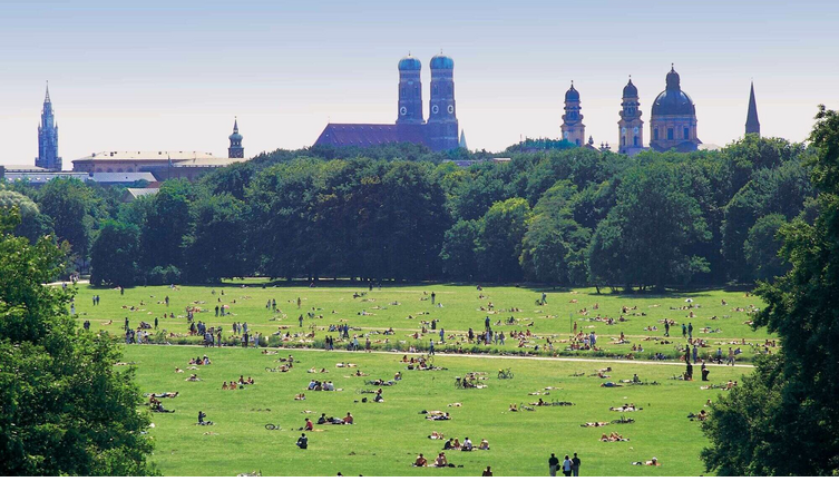 English Garden in Munich Large park with lots of people on a meadow, historic buildings and church towers in the background.